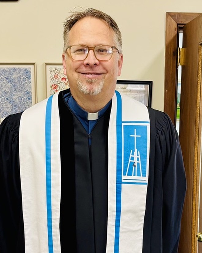 Reverend Ryan Irmer in a black preaching robe and white stole.