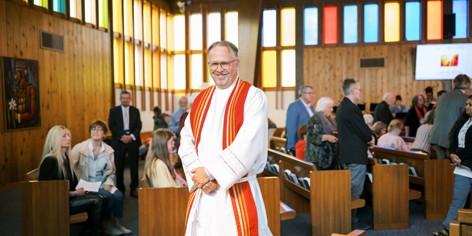 Ryan standing among the pews before a service, with the congregation gathering behind him.