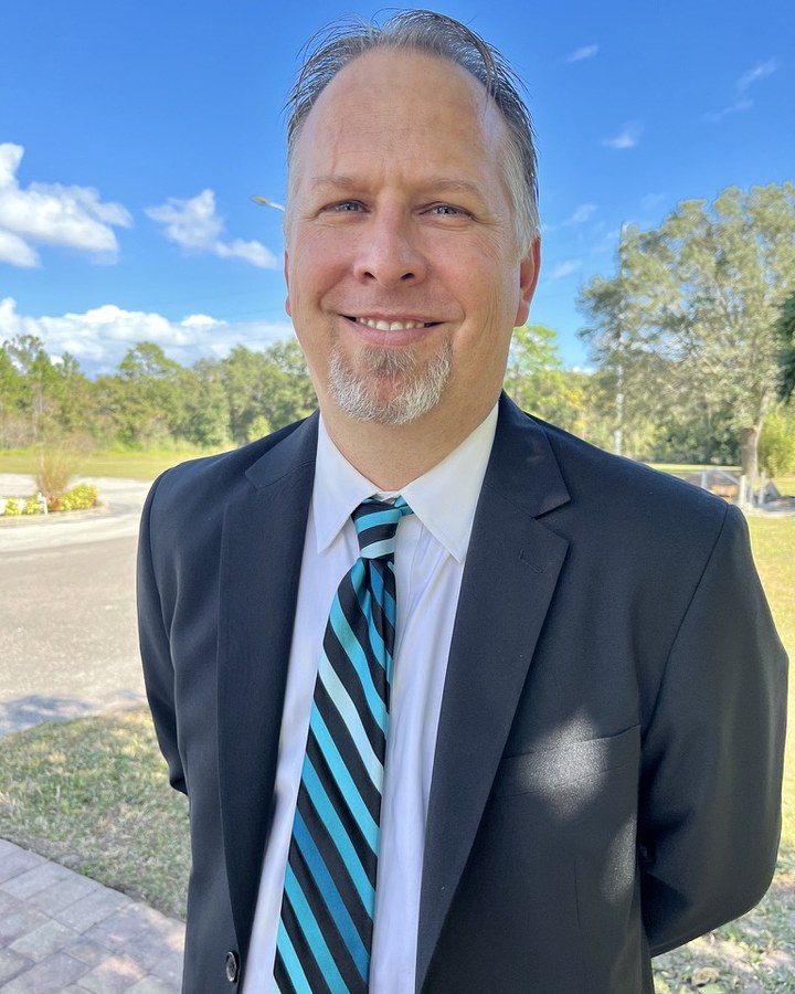 Reverend Ryan Irmer, smiling, in a navy suit and striped tie.